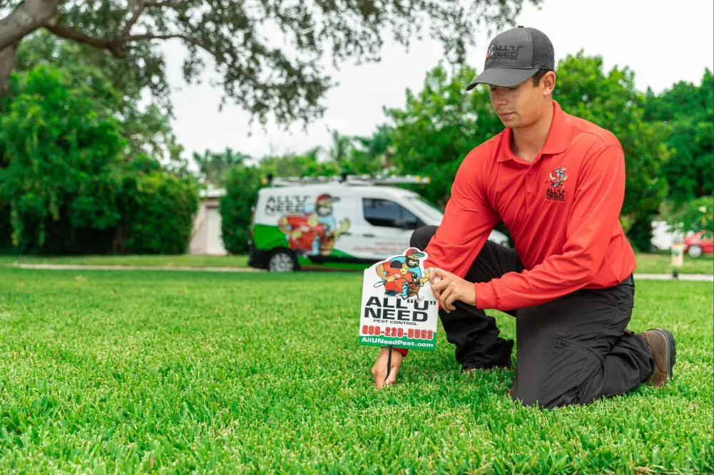 An All U Need Pest Control technician placing a yard sign in front of a home, branded service truck visible in the driveway
